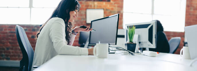 Making successful business plans. Focused young businesswoman smiling while taking a phone call in a modern office. Happy young businesswoman contacting her business clients while sitting at her desk. - JLPSF07657