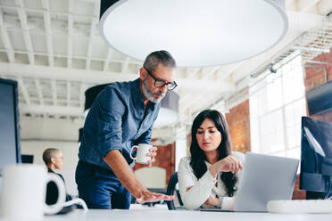 Teamwork in the modern office. Mature businessman having a discussion with his female colleague while standing at her desk in a modern workplace. Two businesspeople working on a project together. - JLPSF07661