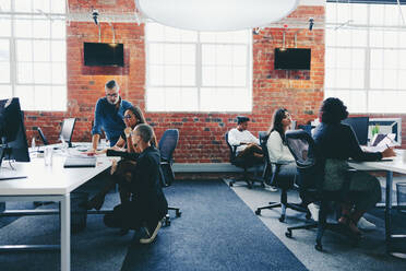 Eine Gruppe von Geschäftsleuten arbeitet in einem kreativen, modernen Büro. Kollegen interagieren miteinander, während sie an ihren Schreibtischen an einem modernen Arbeitsplatz arbeiten. Geschäftsleute arbeiten zusammen und tauschen Ideen aus. - JLPSF07664