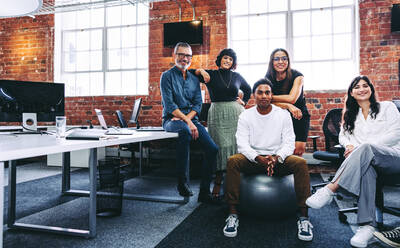 Ein Team von Geschäftsleuten, die in einem kreativen Büro in die Kamera lächeln. Geschäftskollegen, die an einem modernen Arbeitsplatz zusammenarbeiten. Ein buntes Team von Geschäftsleuten, die fröhlich aussehen. - JLPSF07667