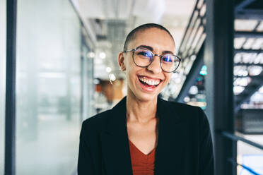 Successful young businesswoman smiling cheerfully. Happy young businesswoman standing alone in a modern workplace. Successful young businesswoman working in a creative office. - JLPSF07680