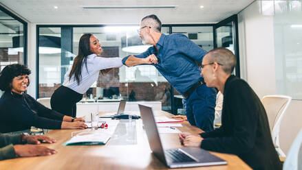 Happy businesspeople elbow bumping each other before a meeting in a boardroom. Group of businesspeople attending a briefing in a modern workplace. Modern businesspeople taking COVID-19 precautions. - JLPSF07705