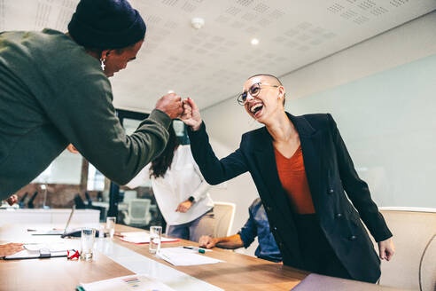 Young businesspeople fist bumping each other before a meeting in a boardroom. Two colleagues smiling cheerfully while greeting each other. Group of businesspeople attending a briefing in a modern office. - JLPSF07709