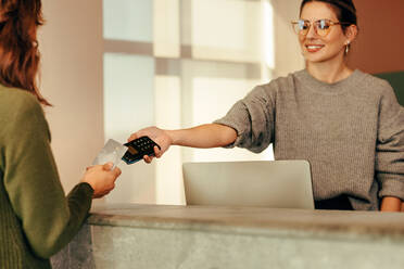 Verkäuferin, die eine Kreditkartenzahlung von einer Kundin entgegennimmt. Glückliche Kleinunternehmerin, die fröhlich lächelt, während sie ihren Kunden an der Kasse hilft. - JLPSF07805