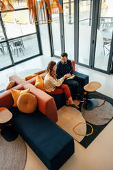 High angle view of two businesspeople working in an office lobby. Two modern businesspeople using a digital tablet while having a discussion. Two young entrepreneurs collaborating on a new project. - JLPSF07836