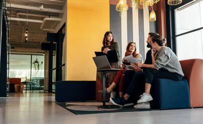 Diverse businesspeople working in an office lobby. Group of happy businesspeople having a discussion while sitting together in a co-working space. Young entrepreneurs collaborating on a new project. - JLPSF07840