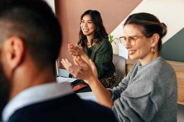 Cheerful businesspeople applauding during an office meeting. Group of multicultural businesspeople clapping happily while sitting in a boardroom. Successful entrepreneurs working together as a team. - JLPSF07844