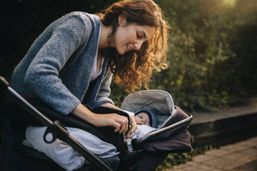 Woman fastening belt on stroller with baby. Mom taking his baby outdoors in a pram. - JLPSF07872