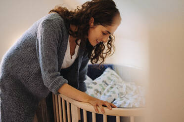 Loving woman putting her baby to sleep in crib. Mother looking after a sleeping baby - JLPSF07887