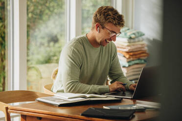 Lächelnder Mann, der an einem Laptop arbeitet. Mann, der zu Hause bleibt, einen Laptop benutzt und lächelt. - JLPSF07891