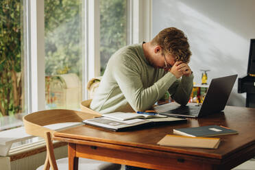 Man feeling stressed while working on laptop. Man sitting at table looking down with hand on head. - JLPSF07892