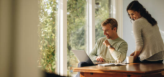 Happy couple enjoying their time at home. Man and woman sitting at tablet looking at laptop. - JLPSF07893