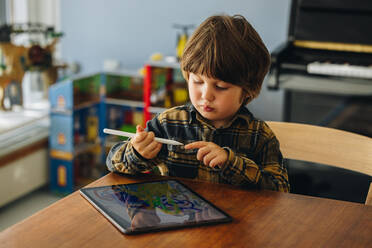 Unschuldiger Junge, der mit einem digitalen Stift auf einem Grafiktablett zeichnet. Kind, das zu Hause ein digitales Tablet und einen Stift benutzt. - JLPSF07908