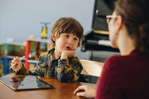 Niedlicher Junge im Gespräch mit seiner Mutter, während er ein digitales Tablet benutzt. Der Sohn unterhält sich mit seiner Mutter zu Hause. - JLPSF07910