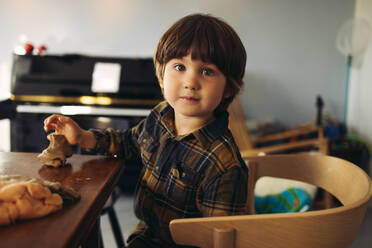 Unschuldiges Kind sitzt am Tisch und spielt mit Knete. Süßer Junge mit Spielknete schaut in die Kamera. - JLPSF07911