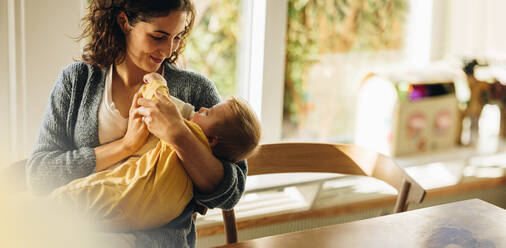 Loving mother feeding baby son with bottle at home. Infant lying on mother's arms drinking milk from a bottle. - JLPSF07912