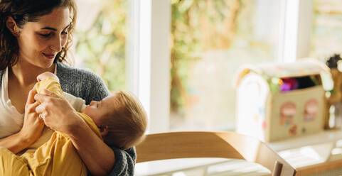 Loving mother feeding her child with baby bottle at home. Adorable baby drinking bottled milk while in arms of his mother. - JLPSF07913