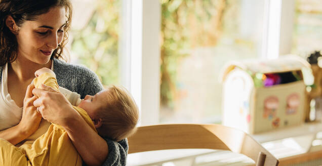 Liebevolle Mutter, die ihr Kind zu Hause mit der Flasche füttert. Süßes Baby, das in den Armen seiner Mutter Flaschenmilch trinkt. - JLPSF07913