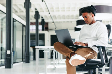 Focused software developer working on a new project. Young businessman using a laptop while sitting in a modern workplace. Creative businessman working alone during the day. - JLPSF07940