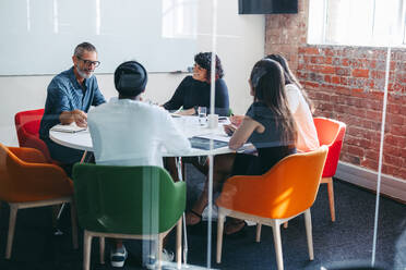 Erfolgreiche Geschäftsleute bei einer Besprechung in einem modernen Büro. Kreative Geschäftsleute, die während ihrer täglichen Besprechung in einem Besprechungsraum fröhlich lächeln. Eine Gruppe von Kollegen, die als Team zusammenarbeiten. - JLPSF07956