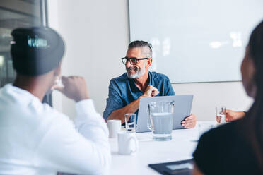 Mature supervisor having a meeting with his colleagues in an office. Experienced businessman smiling while briefing his team in a meeting room. Group of creative businesspeople working together. - JLPSF07959