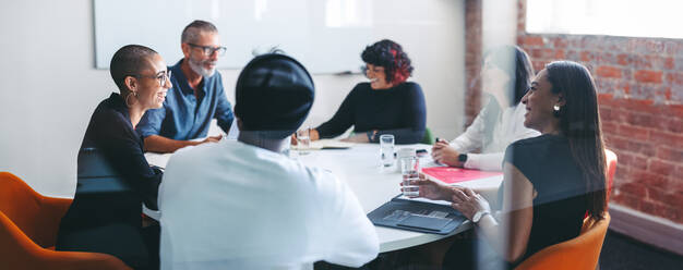 Cheerful businesspeople smiling during a meeting in a modern workplace. Group of successful businesspeople attending their morning briefing in an office. Colleagues working together. - JLPSF07960