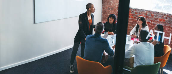 Young businesswoman giving a presentation to her colleagues in an office. Group of creative businesspeople having a meeting in a modern workplace. Businesspeople working together. - JLPSF07966