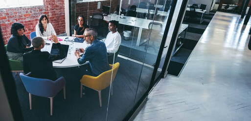 Morgenbesprechung im Büro. Eine Gruppe von kreativen Geschäftsleuten diskutiert während einer Besprechung an einem modernen Arbeitsplatz. Verschiedene Geschäftsleute arbeiten in einem Team zusammen. - JLPSF07969