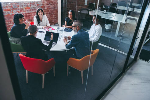 Geschäftsfrau, die eine Sitzung an einem modernen Arbeitsplatz leitet. Selbstbewusste junge Geschäftsfrau, die ihre Kollegen in einem Besprechungsraum unterrichtet. Kreative Geschäftsleute, die in einem Büro zusammenarbeiten. - JLPSF07970