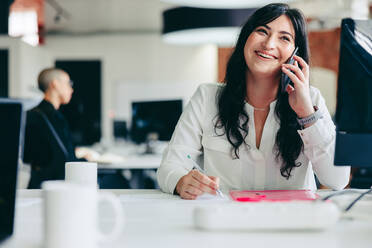 Intelligente Geschäftsfrau, die Geschäftspläne am Telefon macht. Kreative Geschäftsfrau, die mit ihren Geschäftskunden in einem modernen Büro sitzt. Junge Geschäftsfrau, die fröhlich lächelt. - JLPSF08009