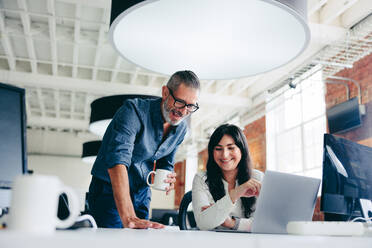 Creative businesspeople making success in the office. Happy mature businessman collaborating with his female colleague in a modern workplace. Two colleagues working on a project together. - JLPSF08013