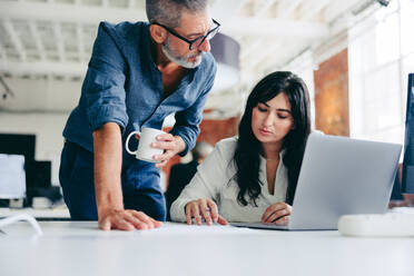 Collaborating on the latest project. Focused mature businessman teaming up with his female colleague in a modern office. Two colleagues having a discussion while going through some paperwork. - JLPSF08015