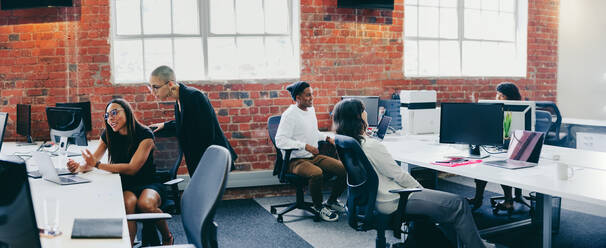 Businesspeople working in a creative modern workplace. Group of young businesspeople interacting with each other while sitting at their desks. Colleagues teaming up and sharing ideas. - JLPSF08018