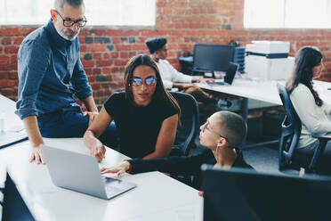 Businesspeople using a laptop while working on a new project together. Colleagues having a discussion and sharing ideas in an office. Group of businesspeople collaborating in a modern workplace. - JLPSF08023