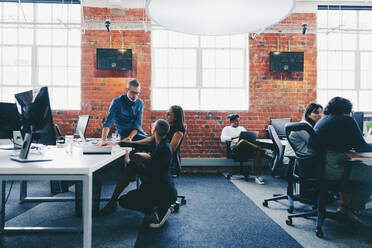 Modern businesspeople working together in a creative office. Group of businesspeople interacting with each other at their desks in a modern workplace. Colleagues collaborating and sharing ideas. - JLPSF08024