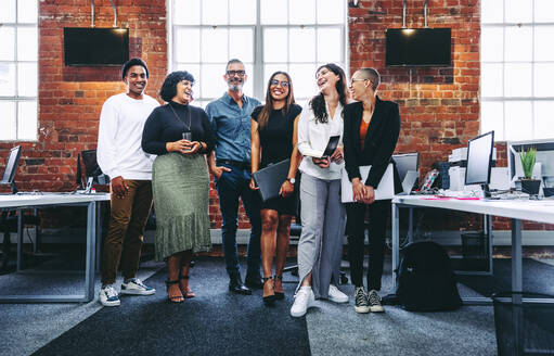 Fröhliche Gruppe von Geschäftsleuten, die an einem modernen Arbeitsplatz fröhlich lachen. Verschiedene Gruppen von Kollegen, die in einem Büro zusammenarbeiten. Erfolgreiche Geschäftsleute, die zusammenstehen. - JLPSF08030