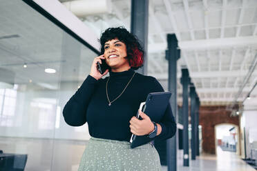 Glückliche Geschäftsfrau, die einen Telefonanruf in einem Büro annimmt. Kreative Geschäftsfrau, die ein Geschäft über das Telefon in einem modernen Arbeitsplatz abschließt. Erfolgreiche Geschäftsfrau, die fröhlich lächelt. - JLPSF08035