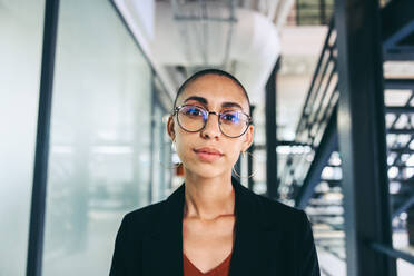 Junge Geschäftsfrau, die in die Kamera schaut. Selbstbewusste junge Geschäftsfrau, die an einem modernen Arbeitsplatz in legerer Business-Kleidung steht. Kluge Geschäftsfrau, die in einem kreativen Büro arbeitet. - JLPSF08043