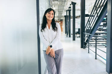 Happy mid-adult businesswoman smiling at the camera. Young businesswoman holding a smartphone while standing alone in a modern office. Successful businesswoman looking cheerful. - JLPSF08047