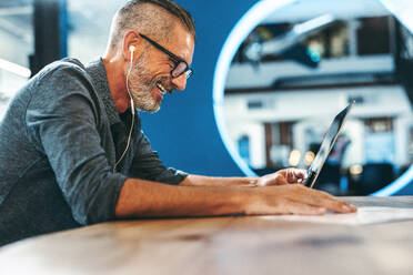 Smiling businessman attending a virtual meeting in a modern office. Experienced entrepreneur using a laptop for a video conference with his partners. Mature businessman sitting in a boardroom. - JLPSF08074