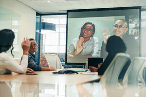 Ein Team von Geschäftsleuten, die ihre Mitarbeiter während einer Videokonferenz begrüßen. Eine Gruppe von Kollegen, die an einem virtuellen Treffen mit ihren globalen Partnern teilnehmen. Geschäftsleute, die eine Besprechung in einem Sitzungssaal abhalten. - JLPSF08079