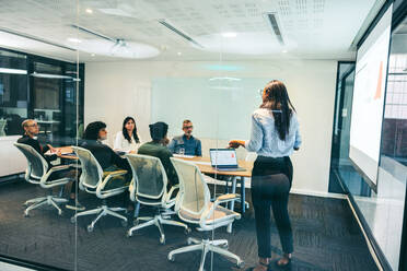 Businesswoman giving a presentation to her colleagues in a modern workplace. Confident businesswoman presenting financial data in a boardroom. Group of businesspeople attending a briefing. - JLPSF08085