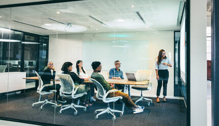 Happy businesswoman giving a financial presentation in a boardroom. Smiling businesswoman presenting statistical details to her colleagues. Group of cheerful businesspeople attending a briefing. - JLPSF08087