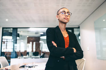 Self-assured businesswoman standing with her arms crossed. Confident young businesswoman looking at the camera in a boardroom. Young businesswoman wearing business casual in a modern workplace. - JLPSF08112