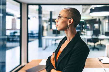 Creative female entrepreneur standing with her arms crossed. Confident young businesswoman looking thoughtful in a boardroom. Young businesswoman wearing business casual in a modern workplace. - JLPSF08113