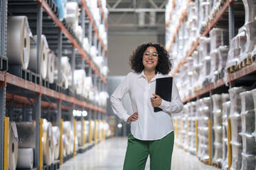 Happy businesswoman with tablet PC standing by rack at warehouse - JOSEF14191