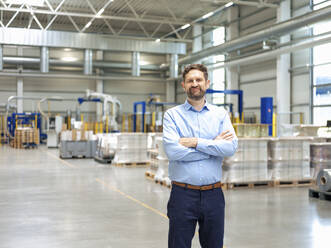 Smiling businessman with arms crossed standing in factory - JOSEF14204