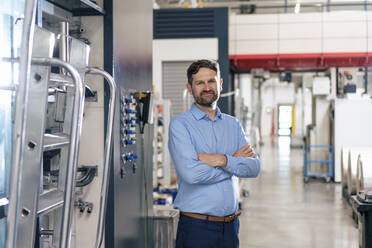 Smiling businessman standing by machine in factory - JOSEF14208