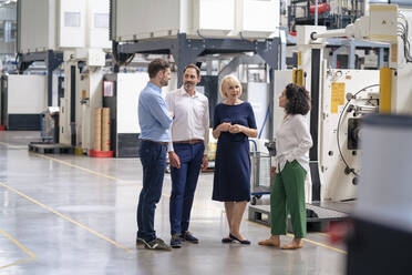 Businessmen and businesswomen discussing in front of machine at industry - JOSEF14223