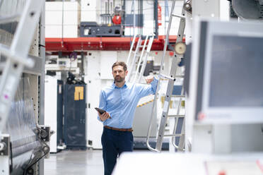 Businessman with tablet PC standing by machinery at industry - JOSEF14274